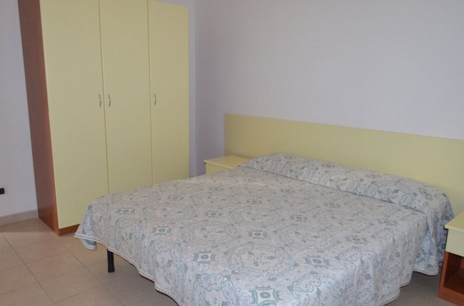 Camera da letto con letto matrimoniale, copriletto decorato, armadio giallo chiaro e comodini.