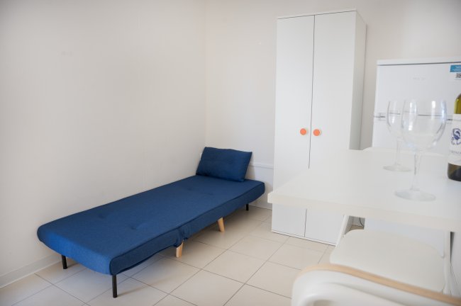 Interno minimalista con letto blu, armadio bianco e angolo bar con sgabelli.