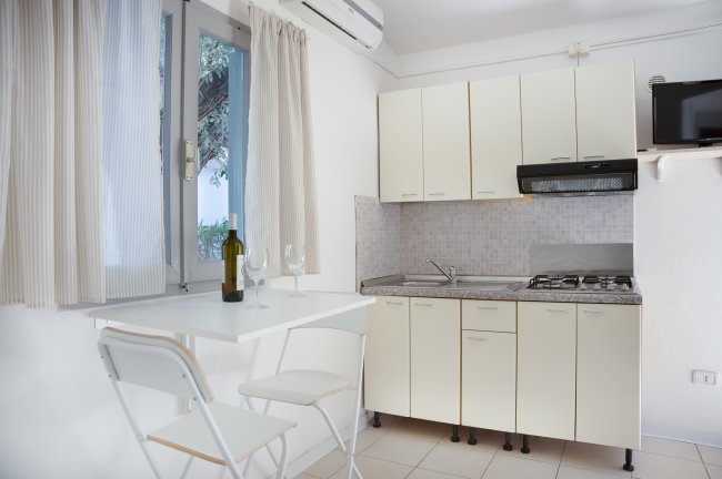 Cucina luminosa con tavolo, sedie pieghevoli e angolo cottura con armadietti chiari.