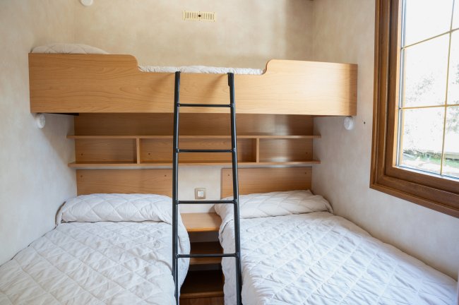 Camera con letto a castello, due letti sotto e scaffali. Finestra a destra.