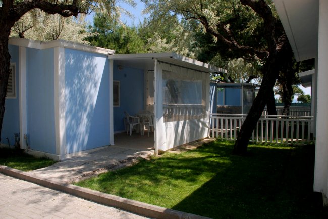 Bungalow blu con veranda ombreggiata e cortile verde.