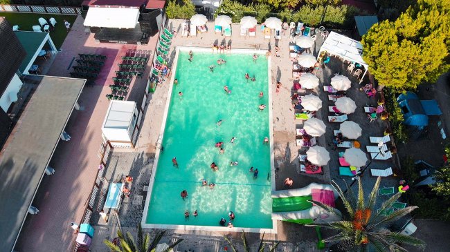 Vista dall'alto di una piscina con persone che nuotano e ombrelloni attorno.