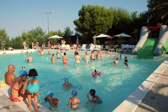 Persone nuotano e si divertono in una piscina all'aperto con scivolo.
