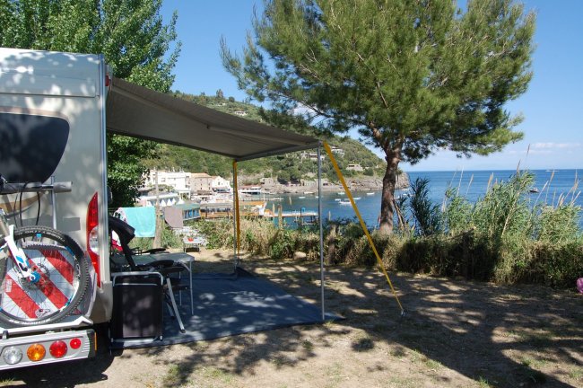 Camper parcheggiato vicino al mare con una bicicletta sul retro e una tenda ombreggiante.
