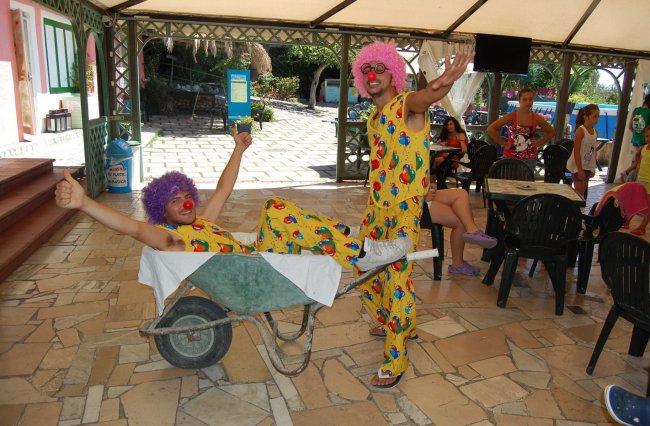 Due clown in abiti colorati, uno su una carriola e l'altro che lo spinge, entrambi sorridenti.