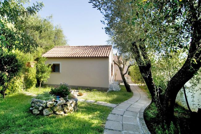 Casa con tetto di tegole rosse, sentiero curvo in cemento, alberi e prato verde.