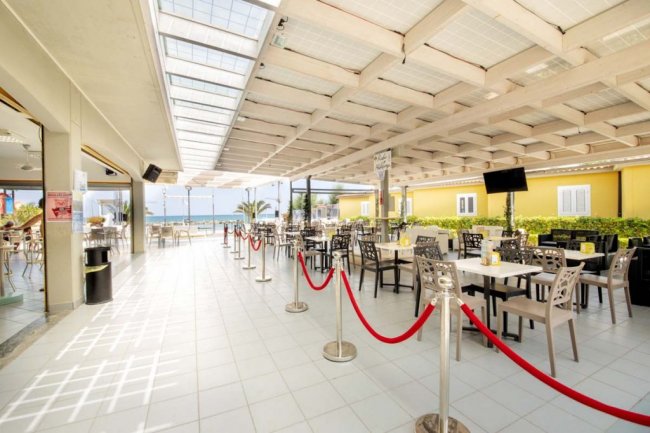 Ristorante all'aperto con sedie nere e corde rosse. Vista mare.