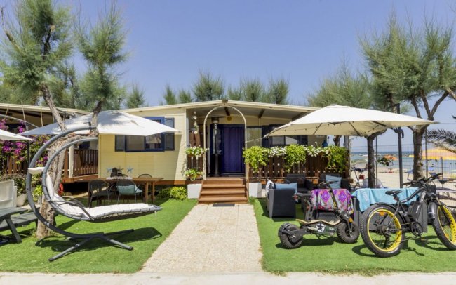Casa su prato con amache, sedie e biciclette; ombrelloni e piante.