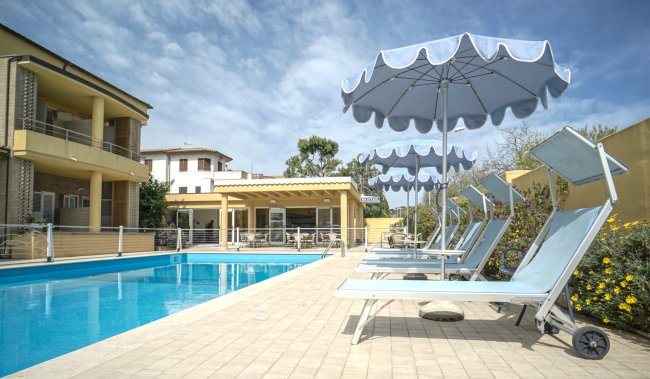 Una piscina con lettini e ombrelloni blu sotto un cielo nuvoloso.