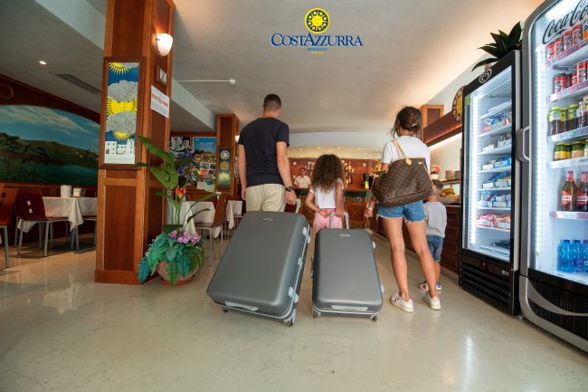 Una famiglia con valigie entra in un hotel, vicino a un frigorifero con bevande.