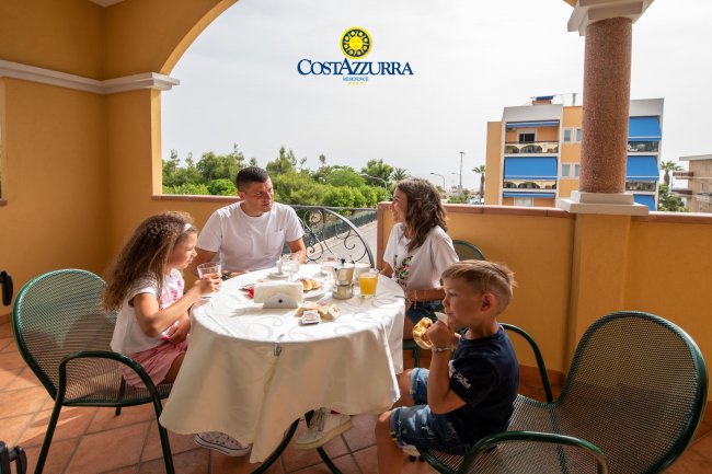 Famiglia seduta a tavola su una terrazza, con bevande e cibo.