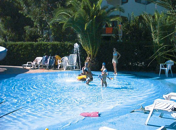 Persone giocano in una piscina poco profonda circondata da lettini e palme.