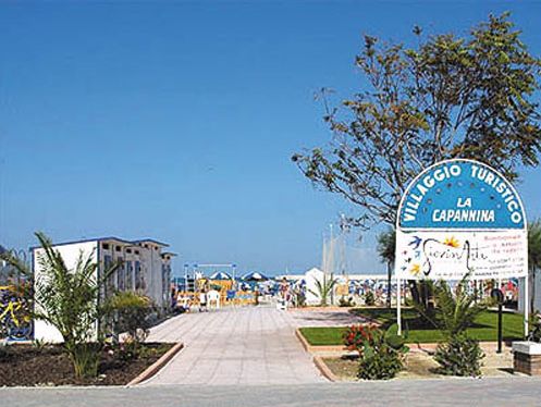 Ingresso del Villaggio Turistico La Capannina con cartello e vista sul mare.