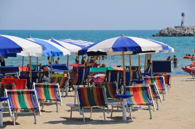 Spiaggia con lettini colorati e ombrelloni blu, mare sullo sfondo.