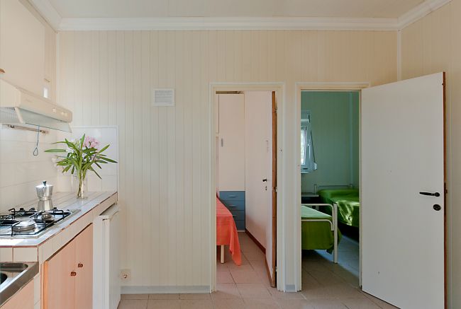 Cucina bianca con porte aperte su due stanze.
