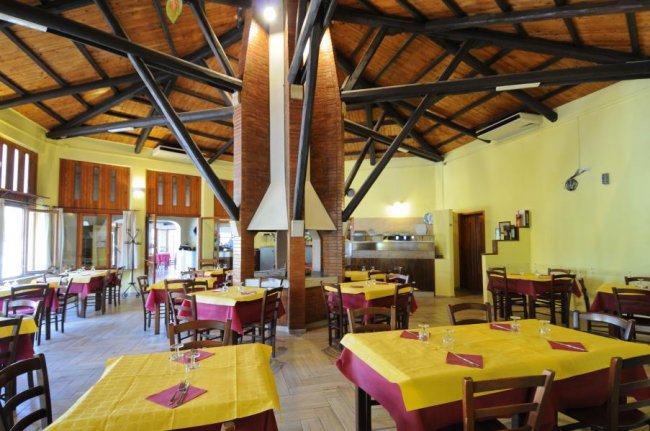 Interno di un ristorante con tavoli apparecchiati, soffitto in legno e travi nere.