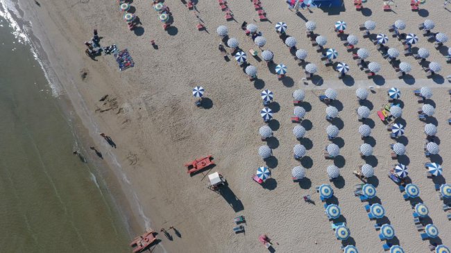 Vista aerea di una spiaggia con file ordinate di ombrelloni bianchi e blu.