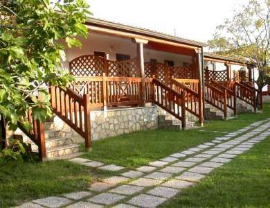 Una veranda di bungalow in legno, con scale e un vialetto in pietra davanti su un prato verde.