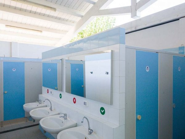 Bagni pubblici con cabine blu e lavandini bianchi sotto uno specchio.