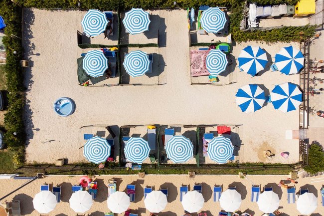 Veduta dall'alto di una spiaggia con ombrelloni blu e bianchi.