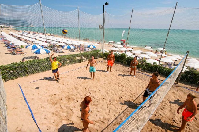 Persone giocano a beach volley su un campo di sabbia vicino al mare.