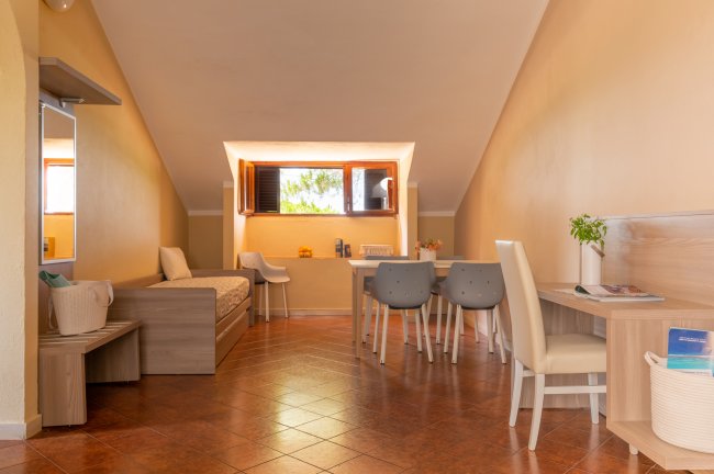 Interno con area pranzo, tavolo e sedie, illuminato da una finestra con vista sugli alberi.
