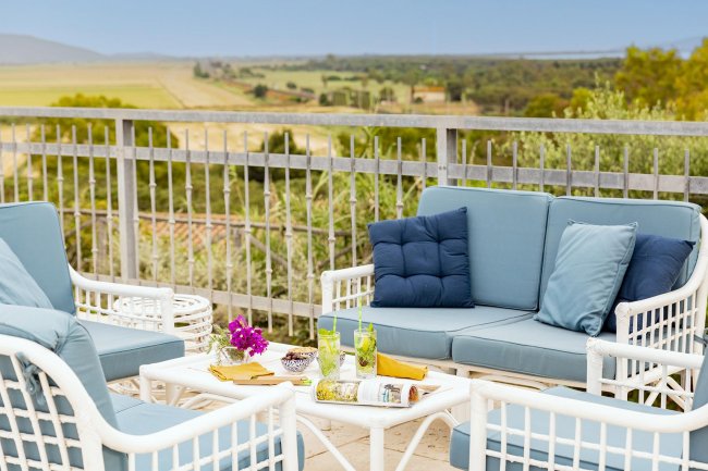 Sala con divani blu e tavolino su una terrazza con vista panoramica su campi e alberi.