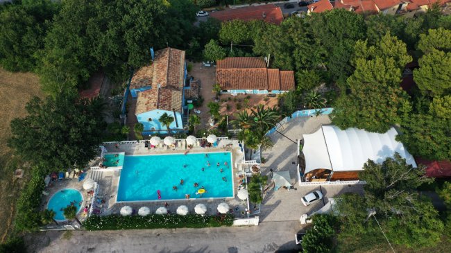 Vista aerea di piscina con ombrelloni e casette.