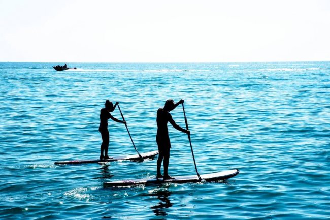Due persone fanno paddleboarding su un mare calmo sotto un cielo luminoso.