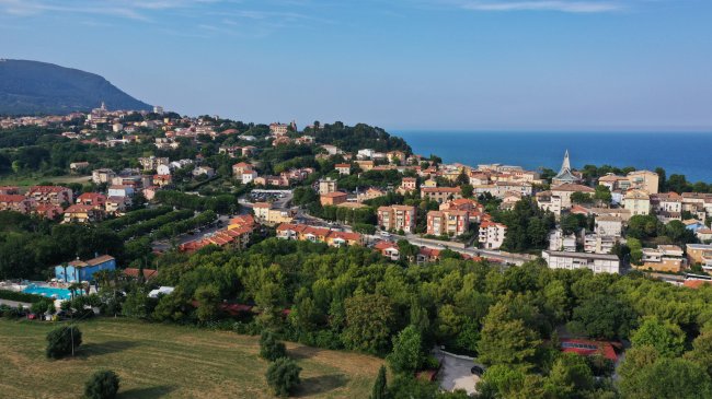 Vista aerea di una città costiera con colline verdi e il mare sullo sfondo.