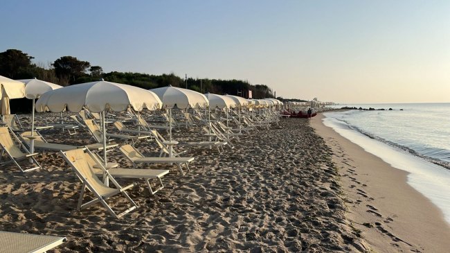 Una spiaggia con file di lettini e ombrelloni vuoti al tramonto.