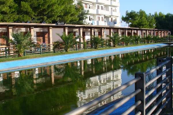 Lungo canale d'acqua con alberi verdi e edificio sullo sfondo.