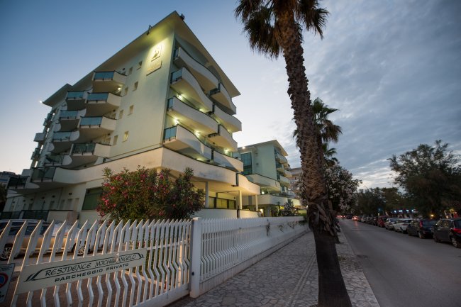 Un edificio residenziale moderno con balconi e palme lungo la strada al tramonto.