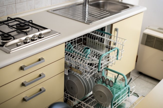 Una lavastoviglie aperta in una cucina con piatti e bicchieri caricati, vicino a un lavandino.