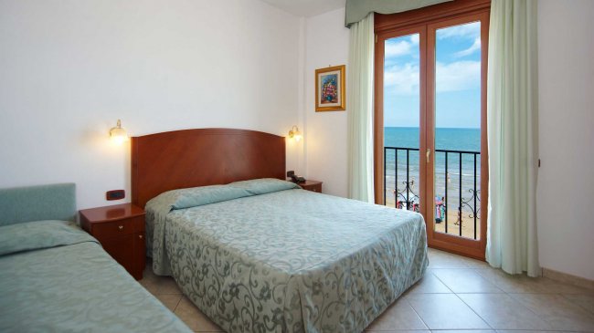 Camera d'hotel con due letti, balcone e vista sul mare.