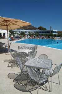 Tavoli e sedie metallici all'aperto vicino a una piscina, sotto un ombrellone.