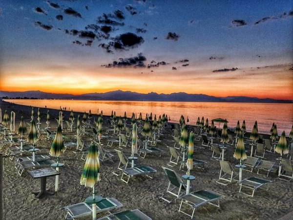 Spiaggia al tramonto con ombrelloni chiusi e lettini vuoti.