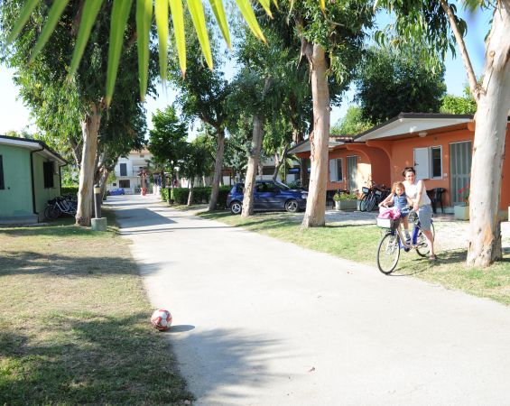 Persona con bambino in bici in un villaggio con alberi e case colorate.