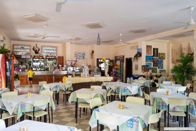 Interno di un ristorante con tavoli apparecchiati, un bancone e pareti decorate con quadri.