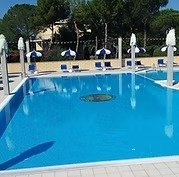 Piscina all'aperto con sedie a sdraio e ombrelloni.