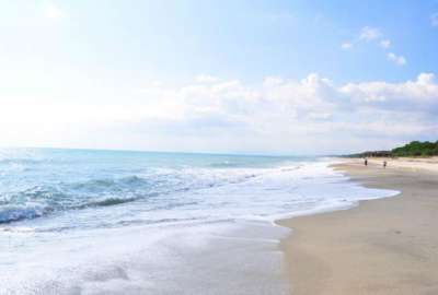 Lunga spiaggia con mare calmo, cielo sereno e poche persone in lontananza.