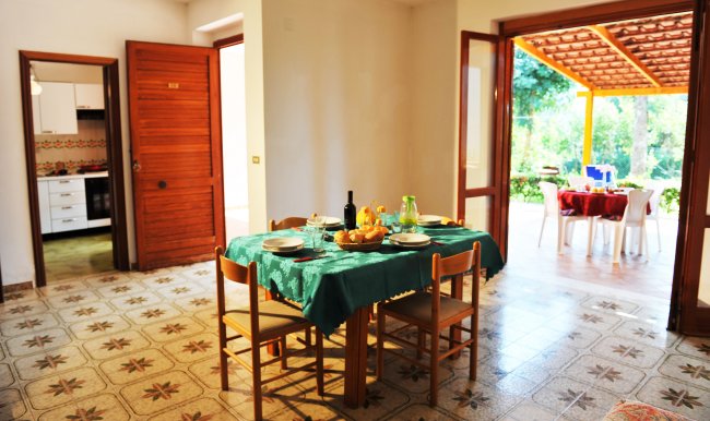 Sala da pranzo con tavolo apparecchiato, cucina e veranda esterna.