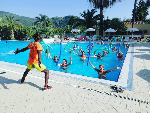 Piscina all'aperto con persone che fanno acquagym. Istruttore in primo piano.