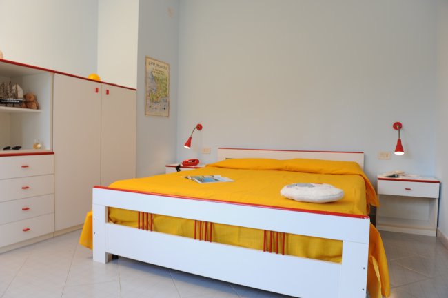Camera da letto spaziosa con arredi bianchi e copriletto giallo.