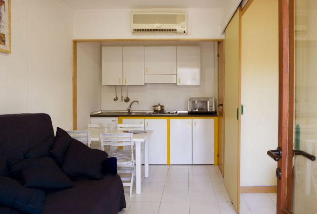 Spazio living con cucina moderna, tavolo da pranzo e divano scuro, evidenziato da pavimenti chiari.