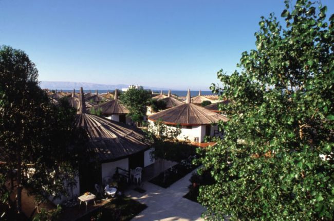 Complesso di bungalow con tetti di paglia, alberi e vista mare.