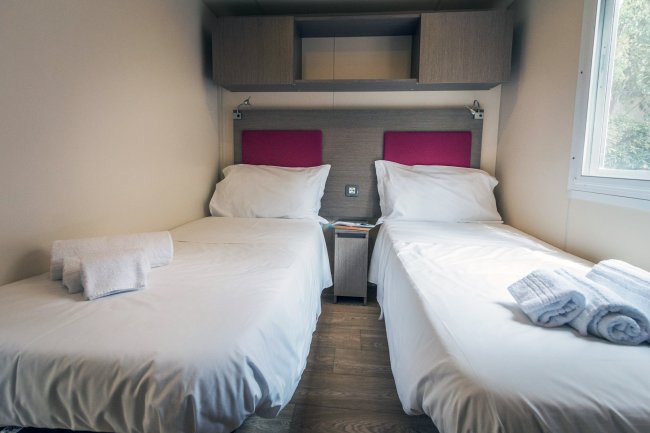 Due letti singoli con lenzuola bianche e asciugamani piegati su ciascun letto.