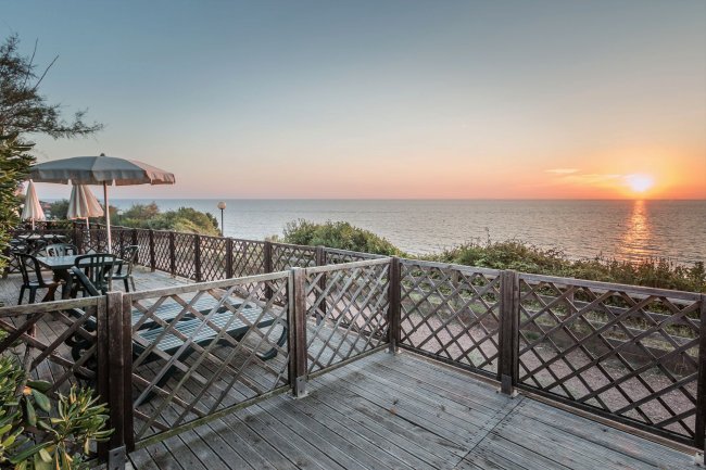Terrazza in legno con sedie e ombrelloni, vista mare al tramonto.