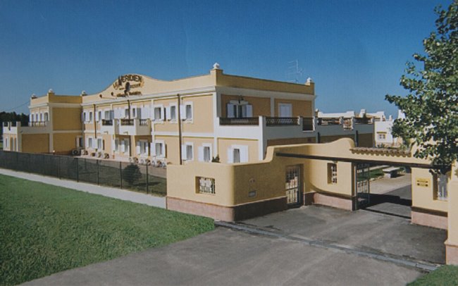Edificio giallo e bianco con cancello d'ingresso e cortile erboso.