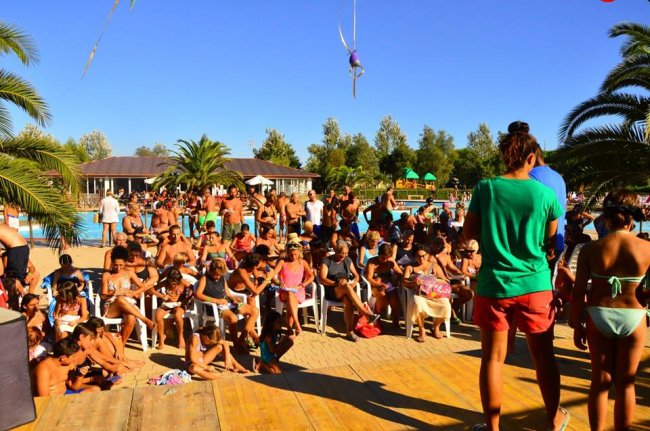 Festa all'aperto con molte persone sedute, intorno a una piscina e palme.